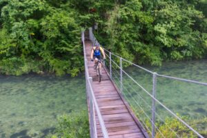 Mountain biker crossing a wooden suspension bridge over the Idrijca River on a guided bike tour in Slovenia