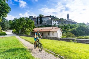 Mountain biker riding below a historic hilltop village, Štanjel, in Karst on a Slovenia mountain bike adventure