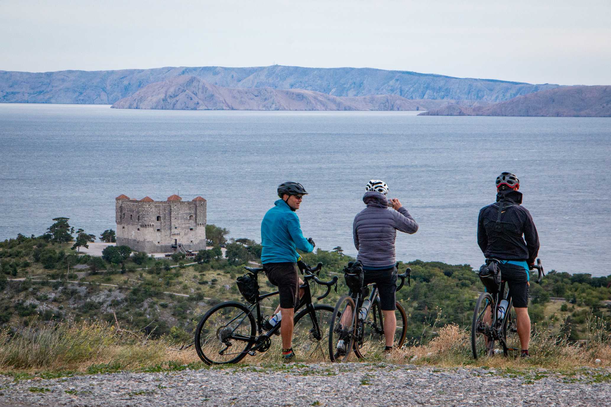 Cyclists overlooking the Adriatic sea and the castle in Senj on Trans Dinarica gravel cycling tour