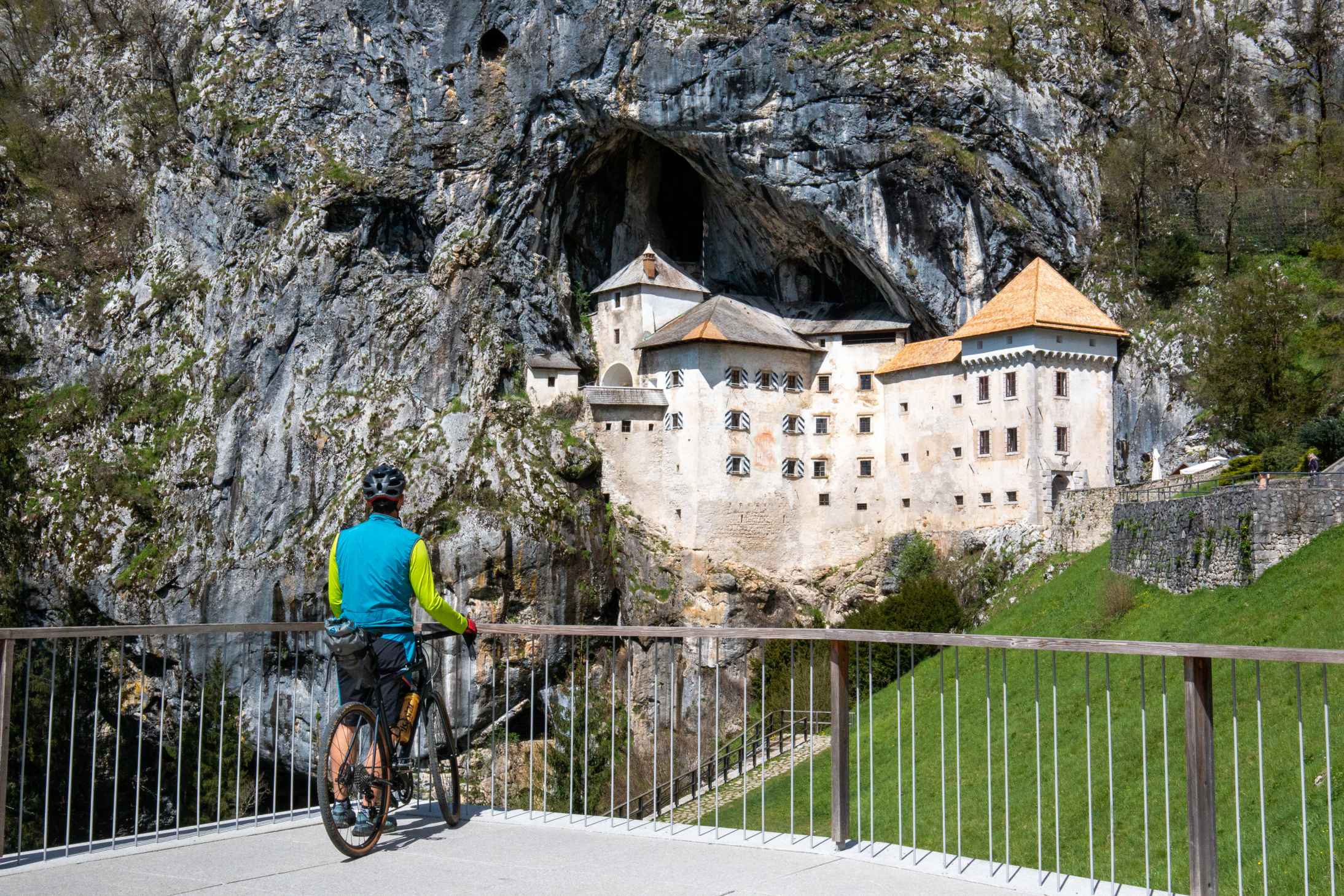 Cyclist overlooking the Predjama Castle on the Trans Dinarica cycling tour in Slovenia
