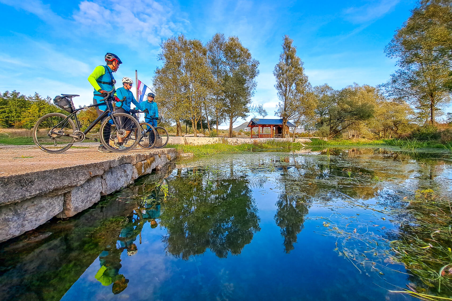Three cyclists enjoy a rest by a small pond in rural Croatia.