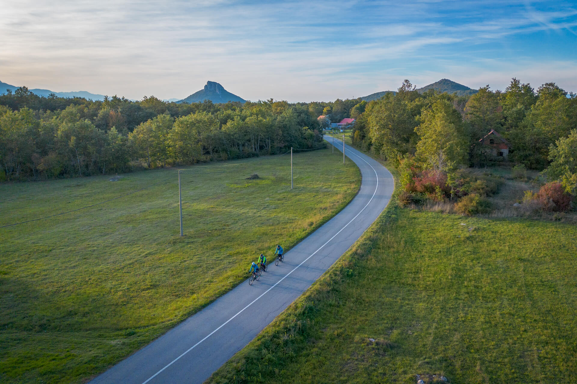 Cyclists on an empty asphalt road in the Lika region, with the interesting rocky mountain Zir in the background.