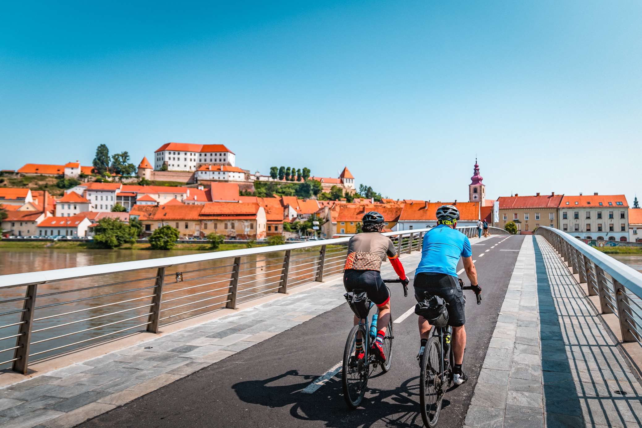 Two cyclists crossing a bridge over the Drava River in Ptuj