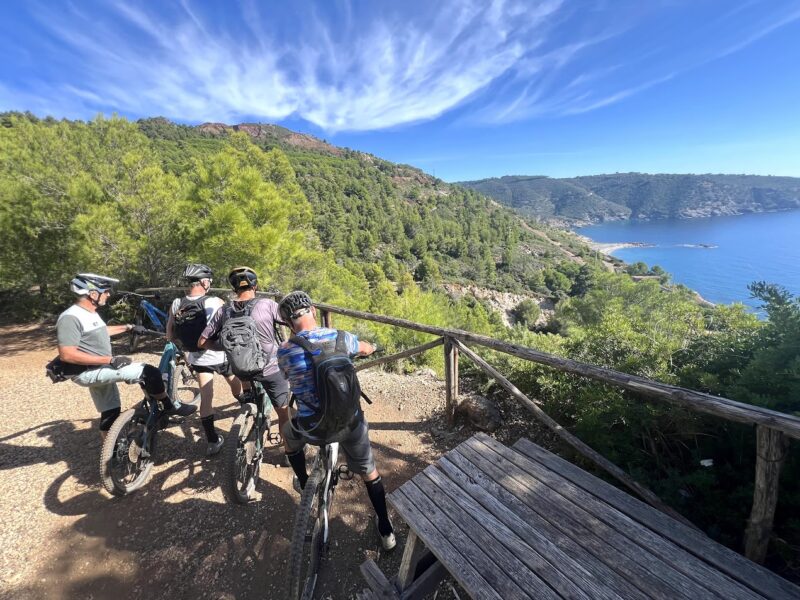 Mountain bikers resting on a forest trail with coastal views during a mountain bike tour in Italy