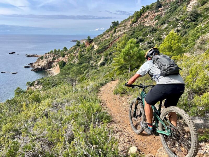 Biker riding a narrow coastal singletrack during an epic MTB tour in Italy